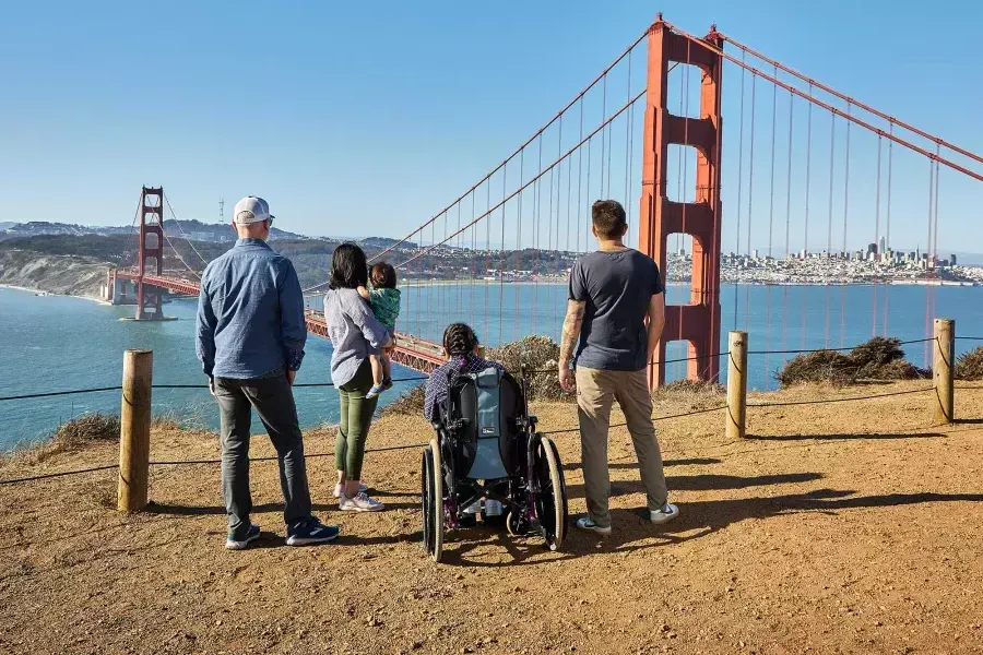 Un groupe de personnes, dont une personne en fauteuil roulant, est vu de derrière alors qu'ils regardent le Golden Gate Bridge depuis les Marin Headlands.