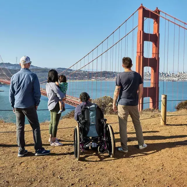 Un groupe de personnes, dont une personne en fauteuil roulant, est vu de derrière alors qu'ils regardent le Golden Gate Bridge depuis les Marin Headlands.